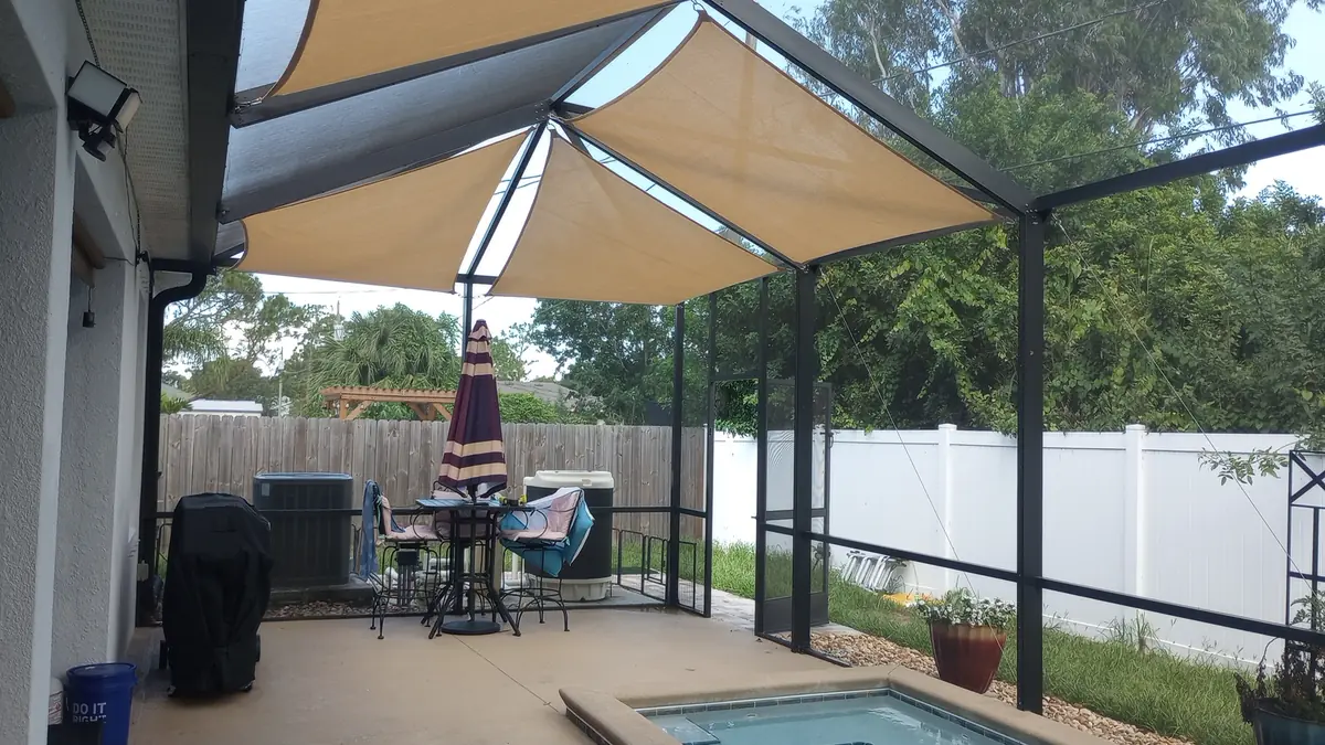 Tan shade sails over a pool patio with a table umbrella in a white screen enclosure